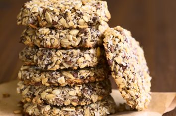 Vegan cookies made of banana, oatmeal and roasted oat grains, linseed, poppy seeds, grated coconut, chia seeds and cinnamon powder arranged in pile, photographed with natural light (Selective Focus, Focus on the front of the cookies)